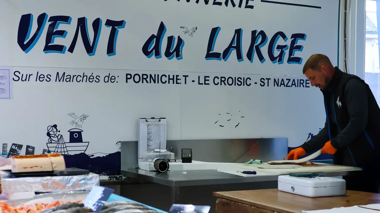 Le poissonnier Vent du Large prépare un poisson derrière son étal de Saint-Nazaire, sous l'enseigne peinte de la poissonnerie